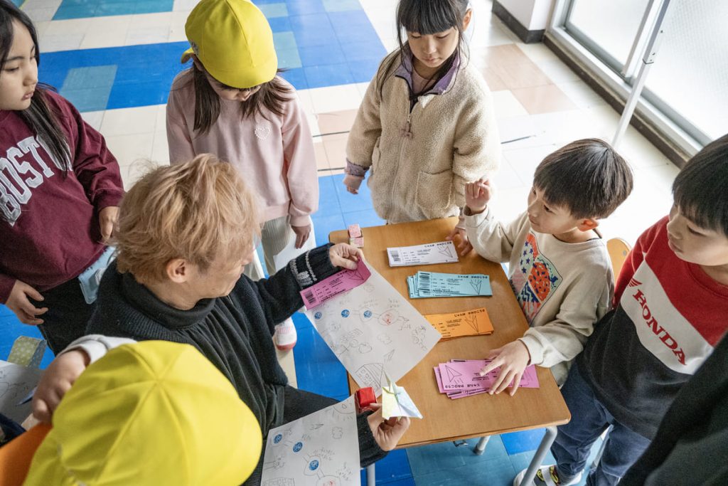 子どもたちから紙飛行機イベントの説明を受けて興奮するつるのさん