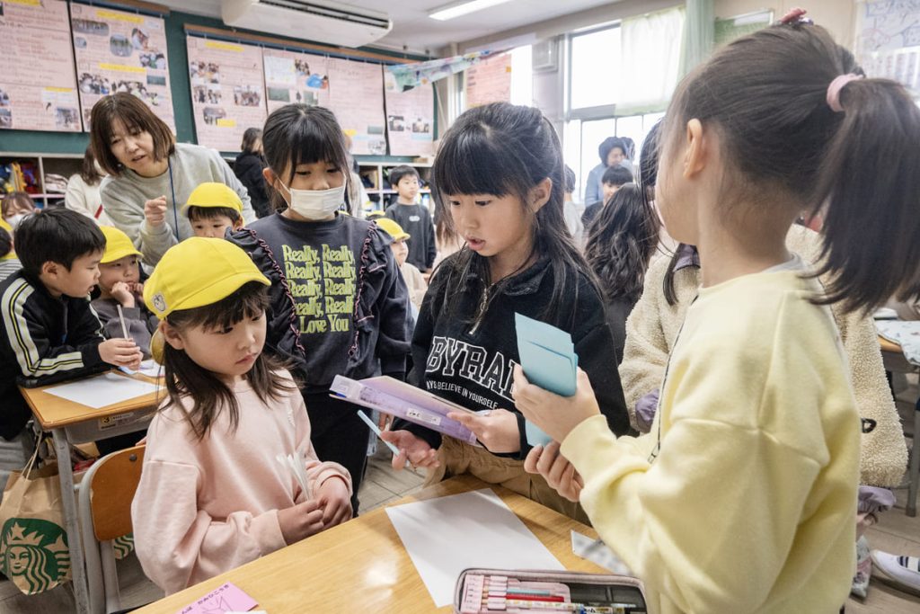紙飛行機に乗って飛んでいきたい場所はどこかと園児たちに聞いて、書き留める1年生。